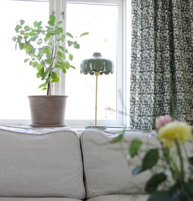 Bild på ljust vardagsrum med soffa, växt och grön bordslampa
