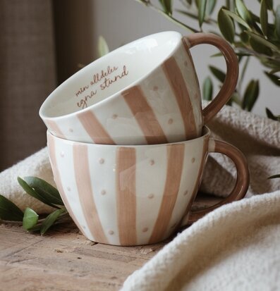 Bild av staplade muggar med beige ränder på rustikt trägolv