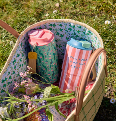 Bild av korg med termosmuggar, blommor och filt på gräs