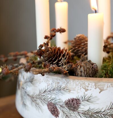 Bild på cremefärgad planteringskruka med tallkvist och ljus