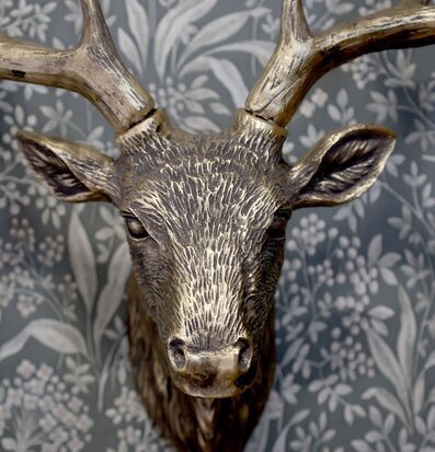 Bild av hjorthuvud i antik mässing mot botanisk tapet
