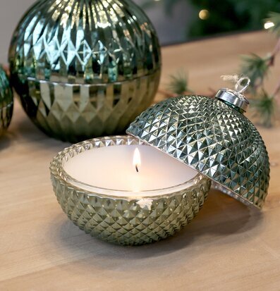 Bild på mossgrön glaskula med tänt ljus och juldekorationer