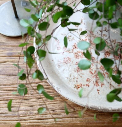 Bild av keramikfat med blommönster på träbord och grön växt