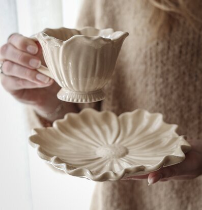 Foto: Beige glaserad kopp och blomformat fat i ljus﻿