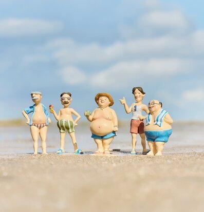 Bild: Fem strandfiguriner på sand med hav och molnig himmel