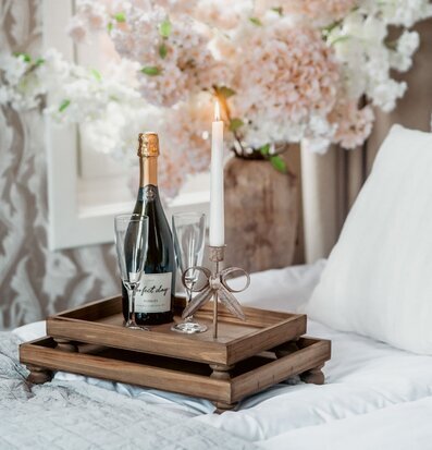 Foto: Träbrickor på säng med champagne, ljus, blommor