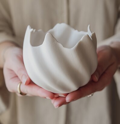 Foto av vit skål med vågig kant i händerna, närbild