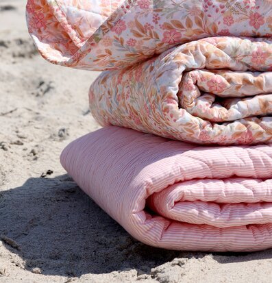 Foto: Rosa/vit quiltad pläd och blommig filt på sand