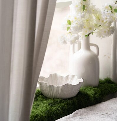 Foto: Vit blomformad skål i fönster med grön mossa