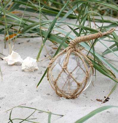 Foto av glaskula i repnät på sand med snäckor