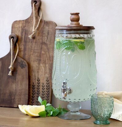 Foto: Glasdispenser med kran, citron och örter på bordet