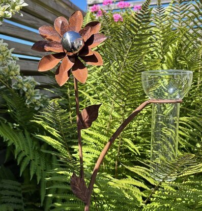 Foto: Regnmätare i glas med metallblomma i grönska