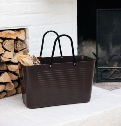 Foto: Brun bärkasse med ved vid vit eldstad inomhus