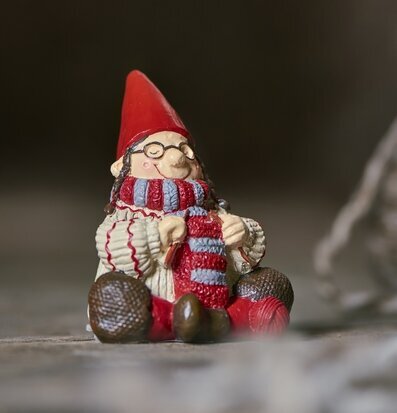 Foto på tomte som stickar med röd luva och glasögon