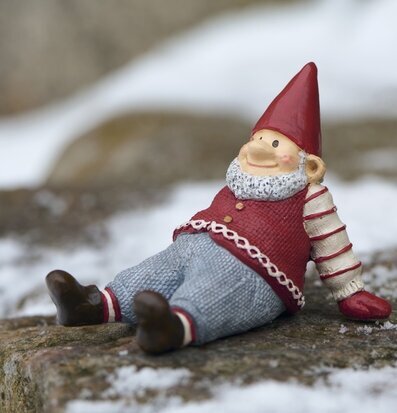 Foto på sittande tomtefigur på sten med snö utomhus
