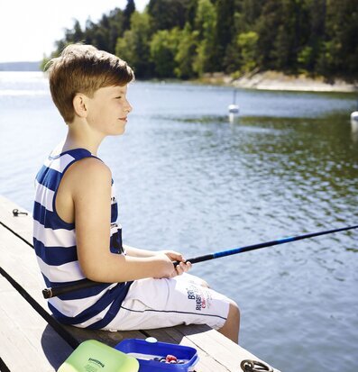 Bild av pojke vid sjön med metspö och somrig picknick